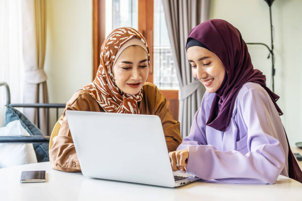 istock Two Asian muslim women wearing hijab using laptop pc for working or watching online content or shopping together in living room at home, respect and collaboration concept. 1400827049