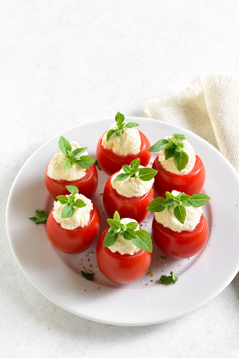 Tomatoes with cream cheese on plate over white stone background. Tasty healthy appetizer. Close up view