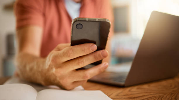 istock Man using a phone while working from home alone. One businessperson working on a laptop and writing in a notebook while using social media on a cellphone and sitting at a table in the morning at home 1400832851