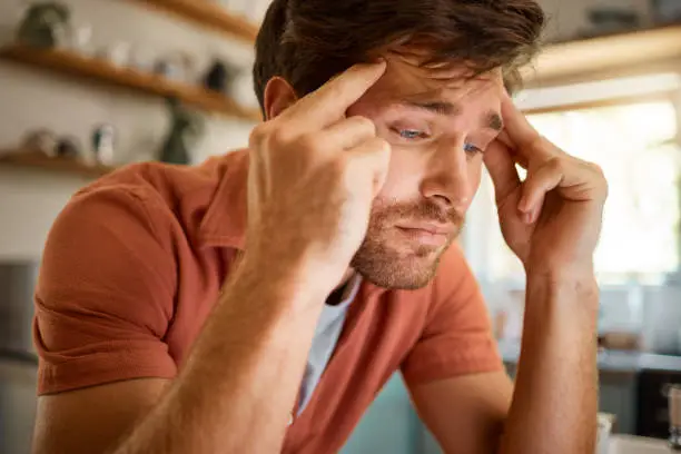 Young caucasian businessman suffering from a headache while working from home alone. One stressed man looking unhappy while working at home. Person looking upset and worried