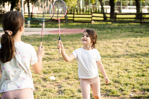 Two little sisters playing badminton at the park and having fun together