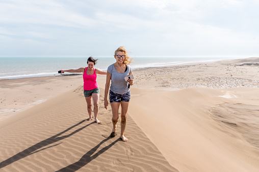 Front view of two women walking on top of a large dune, one of them with arms open to the wind. Mother and daughter.