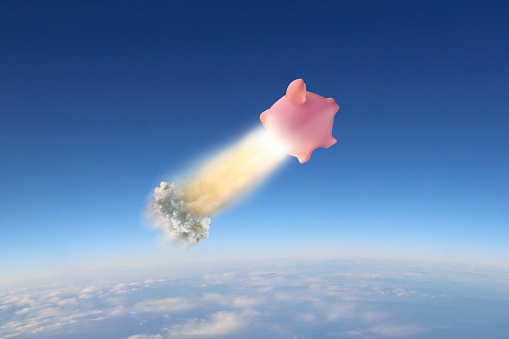 A pink piggy bank takes off like a rocket high above the clouds.
