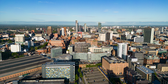 Wide angle aerial view over Manchester city centre, including Piccadilly Station and skyscrapers in the Deansgate area. Early morning sunlight.