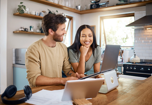 istock Happy young caucasian man working on laptop while his wife stands next to him looking at the screen. Man doing freelance work and getting distracted by beautiful wife 1400838553