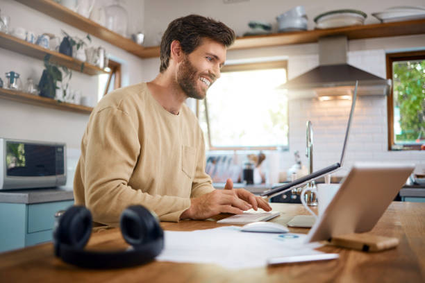istock Smiling caucasian man working on laptop in kitchen, checking his email or searching information while doing freelance work at home. Happy young male using internet banking service 1400838567