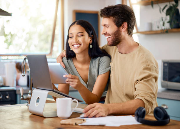 istock Happy young interracial couple calculating their budget using wireless devices at home. Smiling young caucasian man working on laptop while hispanic wife browses social media on digital tablet 1400838573