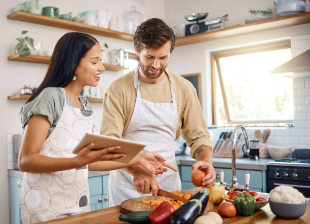 istock Happy young interracial couple using digital tablet while cooking together at home. Young man cutting vegetables while wife explains what to do while reading online recipe. Couple preparing their first meal together 1400838588