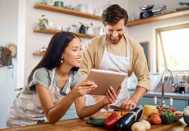 istock Happy young interracial couple using digital tablet while cooking together at home. Young caucasian man cutting vegetables while hispanic wife reads recipe on web 1400838592