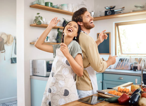istock Cheerful young interracial couple being playful singing and dancing in the kitchen while cooking together. Happy young man and woman wearing aprons and having fun at home 1400838594