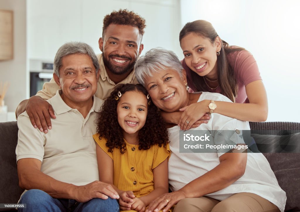 Portrait of mixed race family with child enjoying weekend in living room at home. Adorable smiling hispanic girl bonding with grandparents, mother and father. Happy couples and child sitting together Family Stock Photo
