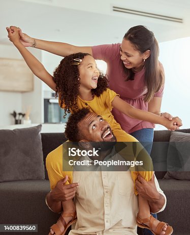 istock Mixed race parents with daughter playing in living room at home. Adorable smiling hispanic girl on father’s shoulders and bonding with mother while pretending to fly. Happy couple and child together 1400839560