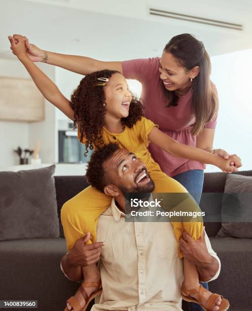 Mixed Race Parents With Daughter Playing In Living Room At Home Adorable Smiling Hispanic Girl On Fathers Shoulders And Bonding With Mother While Pretending To Fly Happy Couple And Child Together Stock Photo - Download Image Now