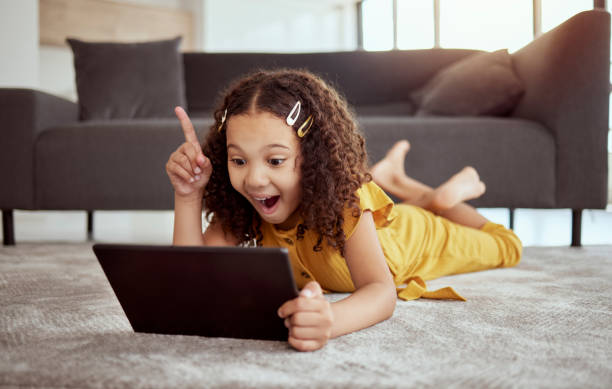 istock Full length adorable little mixed race child using digital tablet and thinking at home. One small cute hispanic girl lying alone on living room floor. Idea and solution while playing technology game 1400839570