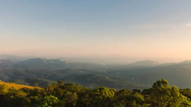 Photo of Cardamom hills under clear sky with mist on horizon at sunset in Thekkady, India.