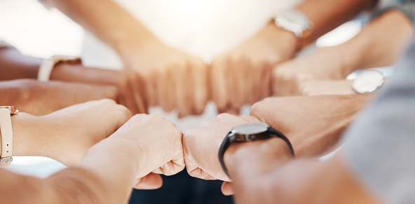 Closeup of diverse group of people making fists in a circle to express unity, support and solidarity. Hands of multiracial community greeting with fist bump in a huddle. Society joining together for collaboration and equality