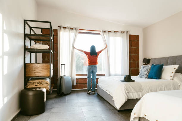 Mature woman entering hotel room and opening window curtains