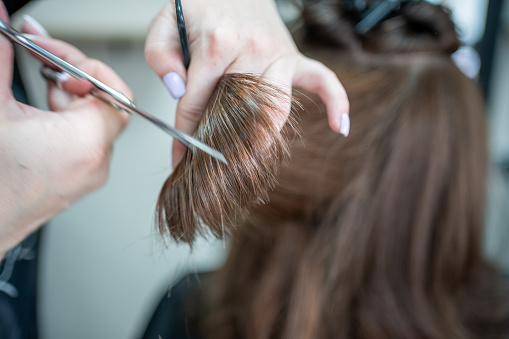 Close up of female hairdresser makes hairstyle on brunette woman in salon, cutting hair with scissors. High quality photo