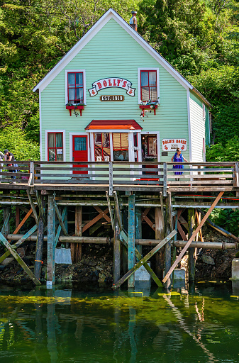 Ketchikan, Alaska, USA - July 17, 2011: Closeup of light green painted Dolly's Museum and gift shop built on stilts at mouth of Ketchikan creek. Green foliage in back. People on boardwalk.