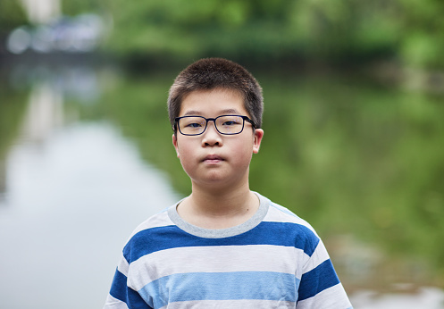 East Asian teenager on a summer trip, looking at the camera with a calm expression by the lake