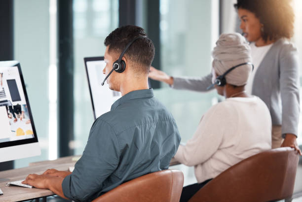 istock Hispanic call centre telemarketing agent from the back talking on a headset while working on a computer in an office alongside his colleagues. Busy consultants operating a helpdesk for customer service and sales support 1400847099
