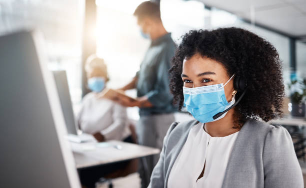 istock Mixed race call centre telemarketing agent wearing face mask as safety protocol and talking on a headset while using computer in an office. Female consultant operating helpdesk for customer service and sales support during covid pandemic 1400847126