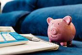 A piggy bank on a blue sofa with a calculator, an open notebook and a pen for notes. Home Finance Concepts, Budget and Expenses.