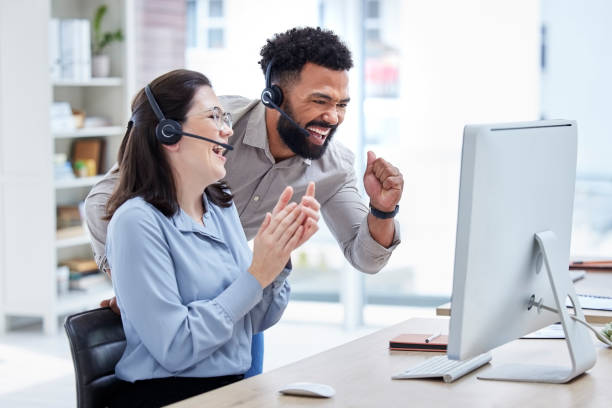 istock Two happy young diverse call centre telemarketing agents cheering with joy while working together on a computer in an office. Excited mixed race man and caucasian woman celebrating successful sales and reaching targets to win 1400847387