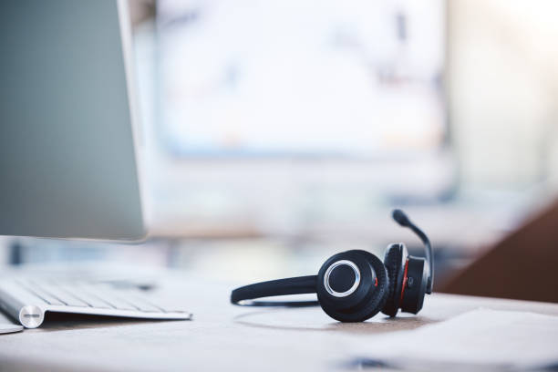 istock Closeup of headset on a table alongside a computer keyboard in an empty call centre office. Operating helpdesk for customer service and sales support. Telemarketing agents providing online assistance 1400847564