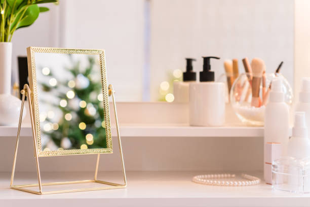 Reflection of christmas tree, light bulbs, in table mirror on woman dressing table with make up accessories stock photo