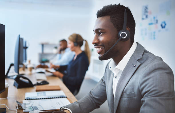 istock Happy young african american call centre telemarketing agent talking on a headset while working on computer in an office. Confident friendly male consultant operating helpdesk for customer service and sales support 1400849597