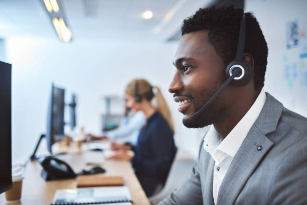 istock Happy young african american call centre telemarketing agent talking on a headset while working on computer in an office. Confident friendly male consultant operating helpdesk for customer service and sales support 1400849617