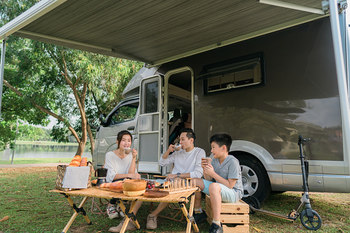 The shot of a happy family taking tea resting, sitting in front of motor home at woodland.