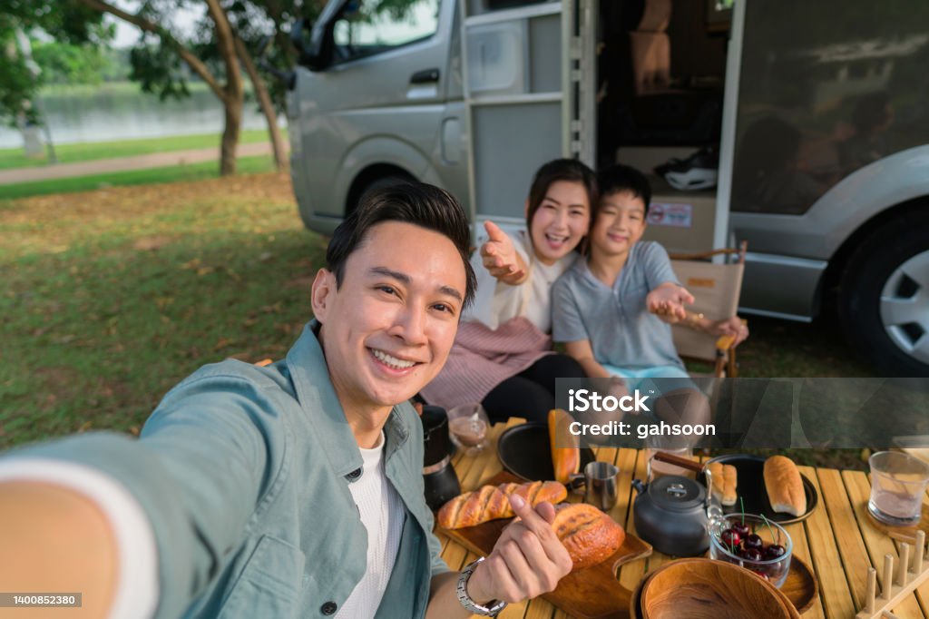 Capturing happy moments of life during vacation trip in motorhome happy family traveling in campervan and picnic outdoor, spending time together while father taking selfie using smart phone, concept of motor home. Family Stock Photo