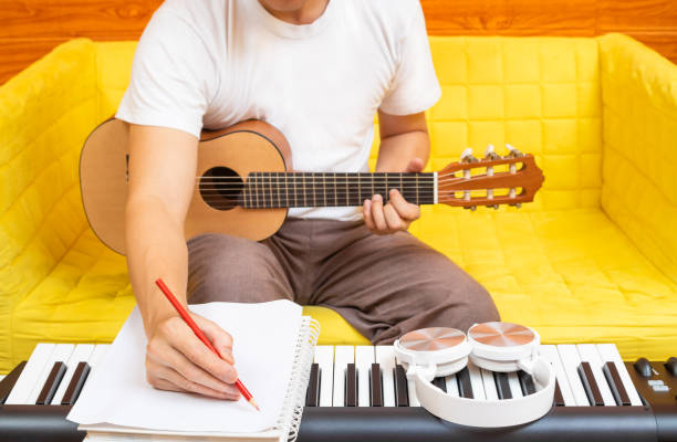 The Best Ways to Find Inspiration for Your Songwriting 9 male amateur songwriter writing a hit song on white paper while playing acoustic guitar in