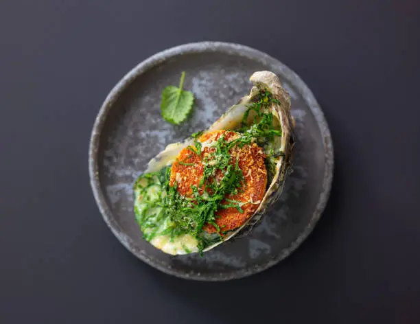 baked oyster with toasted bread and greens on grey plate, top view, selective focus