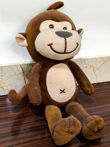 Soft Monkey Toy Brown and light brown cream with tail and hanger kept on golden back, white wall and wooden table sitting position