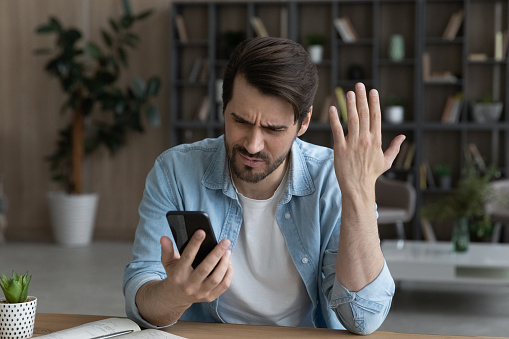 Hombre millennial enojado indignado por el trabajo incorrecto de la aplicación para teléfonos inteligentes photo