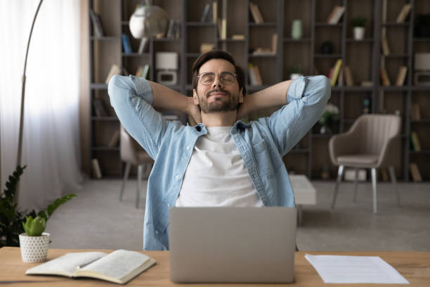 Happy young guy freelancer relax at work desk close eyes Meeting friday. Happy young guy freelancer enjoy calm moment when task is done relax rest stretch back hold hands over head. Serene millennial man recline on chair with closed eyes take break in work meditation room office stock pictures, royalty-free photos & images