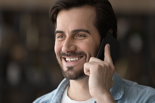 Glad to hear. Happy millennial male listen to praise good news share success personal achievement in phone conversation. Optimistic young guy talk by telephone receive gratitude from satisfied client