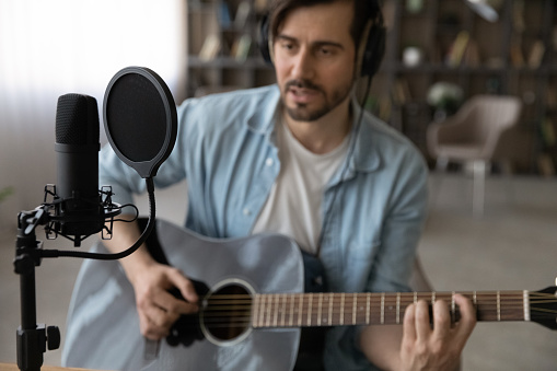 Passionate young male professional guitarist play classic guitar music at domestic studio using special equipment. Focus on sound record accessories condenser microphone in shock mount with pop filter