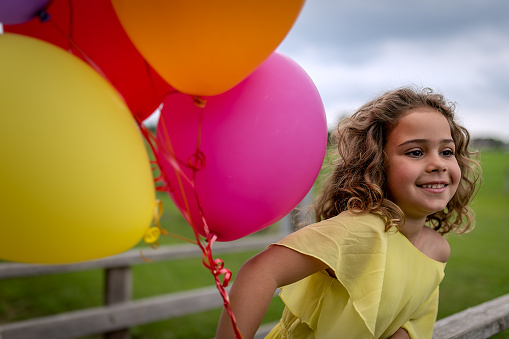A smiling girl in spring nature in a yellow dress, with a wreath of flowers on her head and with colored balloons filled with helium.