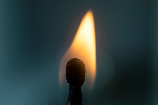 silhouetted hand holding a burning flaming torch over cloudy sky. 