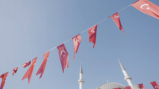 Turkey, Istanbul-December, 2020: Turkish flags on blue sky background. Action. Festive ribbon with Turkish flags fluttering in wind. Turkish flags hang on festive rope on background of minarets.