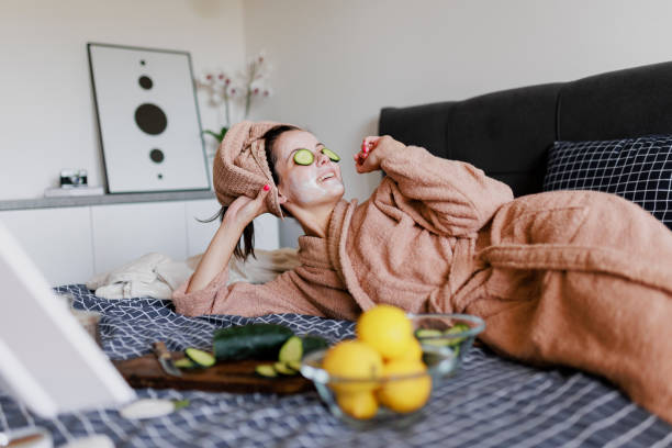 portrait of woman having skin care routine in bed - facial mask spa treatment cucumber human face imagens e fotografias de stock