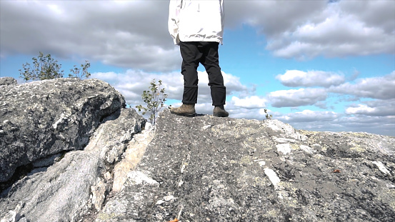 Young man standing on edge of cliff enjoying scenery. Footage. View of man from back on top of cliff. Person engaged in sports has conquered top and enjoys his success.