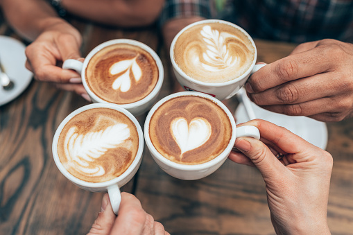 People hands holding cups of cappuccino. Friends drinking coffee together. Hands holding modern looking cups of cappuccino. Tasty and good looking coffee.