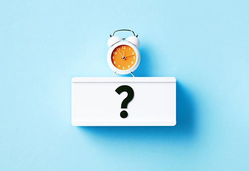 Alarm clock and question mark written white lightbox sitting on blue background. Horizontal composition with copy space.