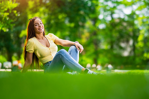 Beautiful young woman relaxing and looking at camera in the park. Vibrant colors on beautiful spring day.