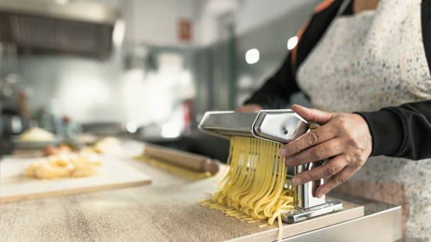 istock Close up female hands preparing preparing fresh fettucine pasta using traditional machine 1400882449